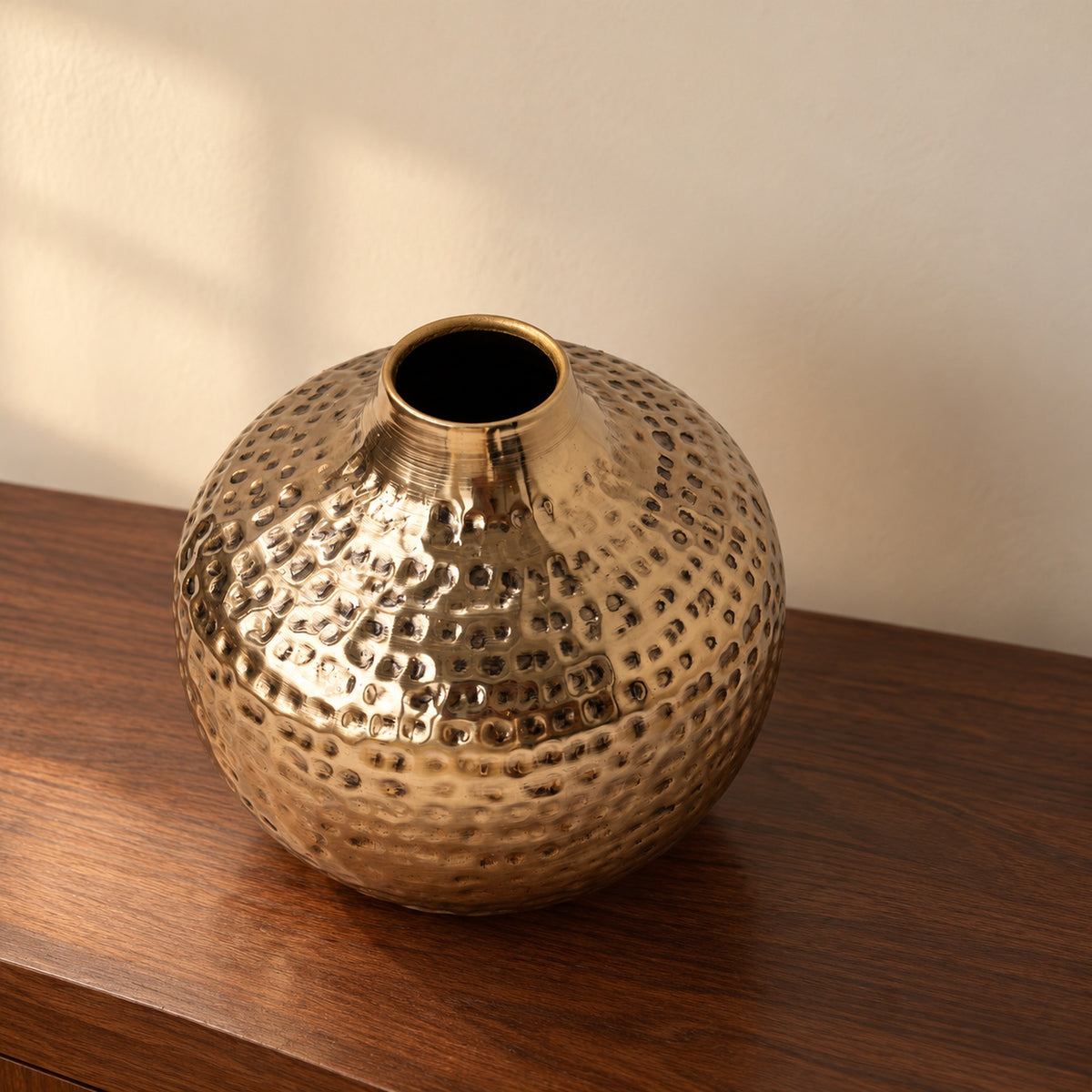 Oria 8 inch hammered champagne gold globe vase seen from slightly above on a walnut console