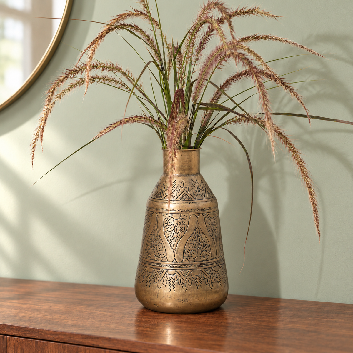 Aurum 12 inch hand-etched antique brass finish vase with dried grass on a walnut console against a bright sage-green wall