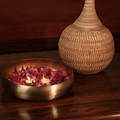 Ekam Metal Urli with rose petals beside a woven vase