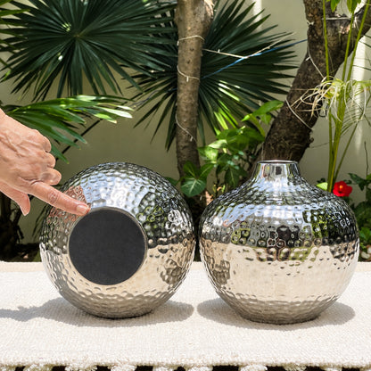 Black felt pad on the base of the Oria hammered silver globe vase, shown in a garden beside a second vase