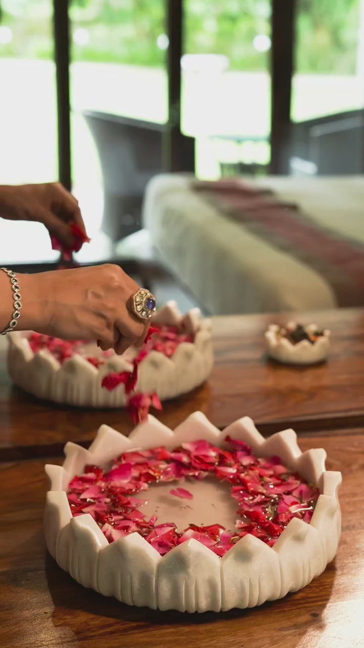 Hands arranging rose petals in a hand-carved white marble lotus bowl